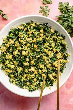 a white bowl filled with pasta and spinach on top of a pink countertop