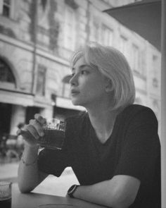 a black and white photo of a woman sitting at a table with a drink in her hand