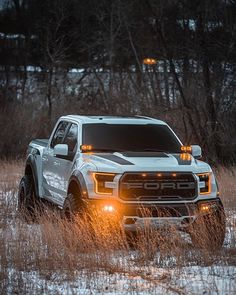 a white truck parked in the middle of a field with its lights on at night