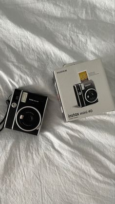 a black and white camera sitting on top of a bed next to an open box