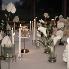 the table is set with candles, flowers and vases in glass containers on it