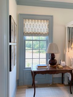 a room with a table, lamp and pictures on the window sill in it