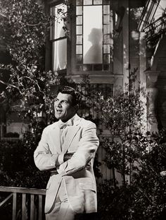 a man in a suit and tie standing on a porch with his arms folded up