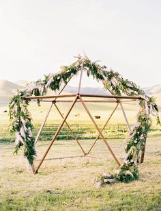 a wooden structure decorated with greenery and flowers in the middle of a grassy field