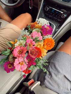 a bouquet of flowers sitting in the center console of a car with someone's feet on the steering wheel