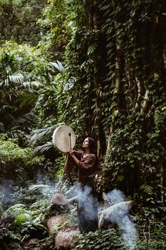 a woman standing in the middle of a forest holding a frisbee above her head