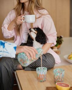 a woman sitting at a table with her dog drinking from a cup while holding a tea bag