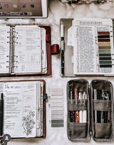 an open planner, pen and pencil holder on a marble table with various items in it