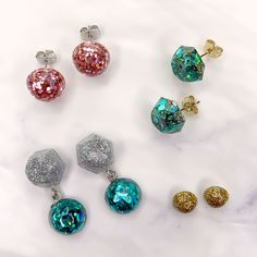 five different colored earrings on a marble surface with gold, silver and blue glitters