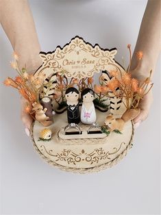 a person holding a small figurine on top of a wooden box filled with flowers