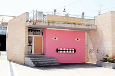 a pink building with a face painted on it's side and stairs leading up to the entrance