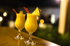 two glasses filled with yellow liquid sitting on top of a wooden table next to each other