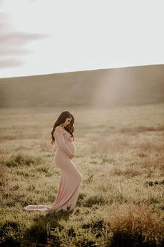 a pregnant woman standing in a field with the sun shining down on her head and arms behind her back