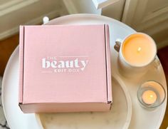 a pink beauty box sitting on top of a white plate next to two lit candles