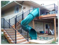 a green slide sitting in front of a house next to a metal stair railing and wooden deck