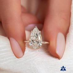 a woman's hand holding an engagement ring with a pear shaped diamond on it