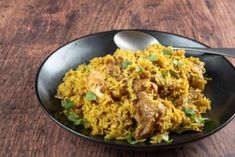 a black bowl filled with rice and meat on top of a wooden table next to a spoon