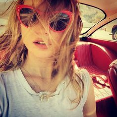 a woman wearing sunglasses sitting in the back seat of a car with her hair blowing in the wind