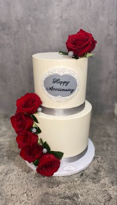 two tiered wedding cake with red roses on the top and happy anniversary written on it