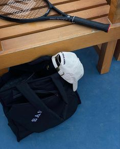 a tennis racquet and bag sitting on the ground next to a wooden bench