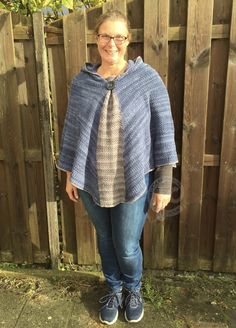 a woman standing in front of a wooden fence wearing a blue sweater with a tie