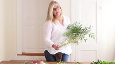 a woman kneeling down in front of a table with flowers and plants on top of it