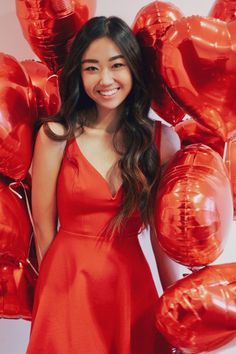 a woman in a red dress posing for a photo with balloons around her and smiling at the camera