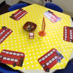 the table is covered with yellow and white polka dot paper, which has red double decker buses on it