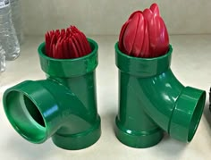 two green vases with red flowers in them sitting on a white counter top next to water bottles