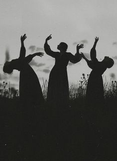 three people standing on top of a grass covered field with their arms in the air