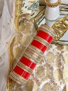 red and gold bracelets sitting on top of a table next to a white vase