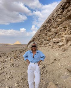 a woman standing in front of a pyramid with her hands on her hips while wearing white pants