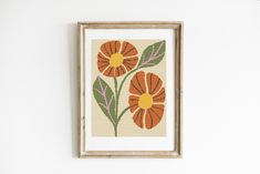 an orange and green flower cross stitch pattern on a white wall above a wooden frame