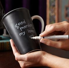 a woman holding a coffee mug with writing on it and a marker in her hand