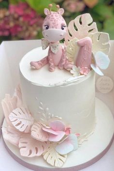 a white cake with pink decorations and a giraffe figurine on top