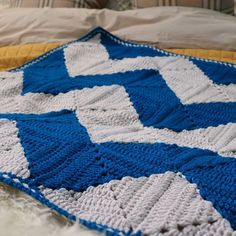 a blue and white crocheted blanket on top of a bed next to pillows