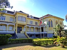 a large yellow building with two flags on it's roof and stairs leading up to the second floor