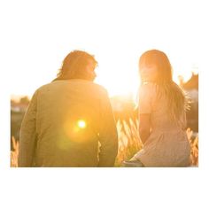 a man and woman walking in the grass at sunset with the sun shining behind them