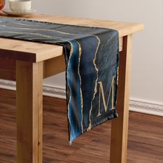 a wooden table topped with a black and gold table runner next to a bowl of fruit