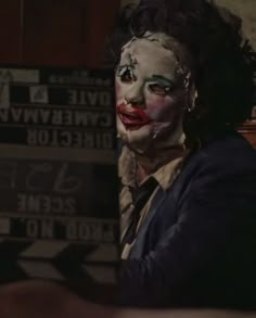 a man with clown makeup on his face sitting in front of a wooden signboard