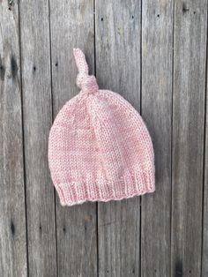 a pink knitted hat hanging on the side of a wooden fence next to a piece of wood