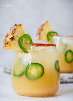 two glasses filled with cucumber and pineapple margaritas on top of a table