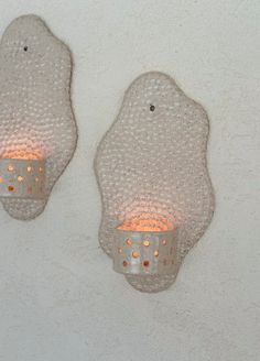 two wall mounted lights on the side of a white wall next to each other with holes in them