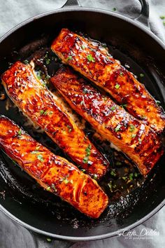 salmon fillets cooking in a skillet on a table with green onions and parsley