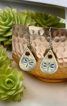 a pair of earrings with dragonflies on them sitting next to a potted plant