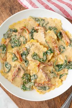 a white plate topped with pasta and spinach covered in sauce on top of a wooden table