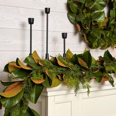 a wreath is hanging on the mantle with candles and greenery in front of it