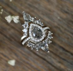 a diamond ring sitting on top of a wooden table next to white and gray flowers