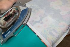 someone is ironing something on top of a bed with a flowered sheet behind it