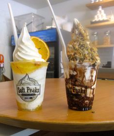 two ice cream sundaes sitting on top of a wooden table next to an orange slice